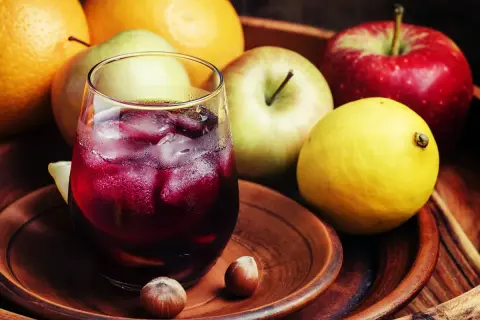 Un refrescante tinto de verano con espuma de limón, rodeado de frutas frescas como naranjas, manzanas y un limón amarillo.