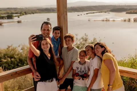 Familia sonriente se toma un selfie con un lago de fondo. Un día perfecto en la playa de Vera para niños, explorando la naturaleza.