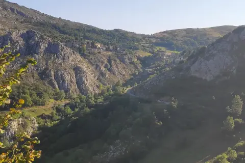Malowniczy widok na dolinę z krętą drogą, domkami na zboczu i skalistymi górami. W oddali majaczy szczyt Naranjo de Bulnes.