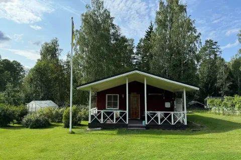 Rött hus med veranda och flaggstång i Stjärnsund. En växthus syns i bakgrunden.