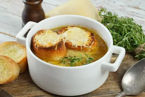 Jak zrobić zupę cebulową? Aromatyczna zupa cebulowa z grzankami i serem, podana w białej miseczce, z gałązką tymianku.