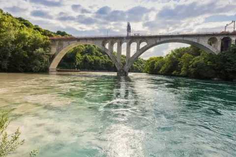 Ponte ad arco su fiume con acque di colori diversi, dove si intravedono segnali navigazione fluviale.