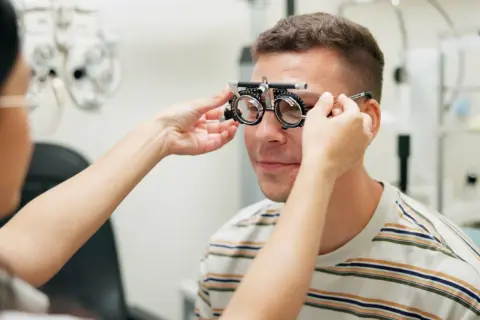 Okulista dopasowuje soczewki próbne mężczyźnie. Idealny moment, by skorzystać z promocji na okulary i zadbać o wzrok.