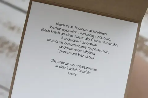 Wiersz z życzeniami "100 lat wszystkiego najlepszego z okazji urodzin" na kartce z brązowej tektury.