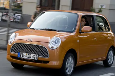 Pomarańczowy Daihatsu Trevis z kierowcą za kierownicą jedzie ulicą.