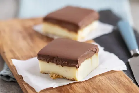 Zwei rechteckige Stücke schokokuchen mit vanillepudding, bedeckt mit Schokolade, auf einem Holzbrett.