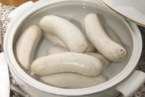 Biała kiełbasa w garnku z wodą, gotowa do parzenia. Delikatne kiełbaski czekają na idealny moment.