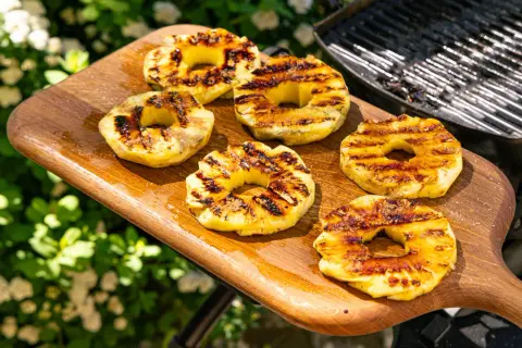 Gegrillte Ananasscheiben mit karamellisierten Rändern auf einem Holzbrett, bereit zum Servieren. Das Ananas grillen bringt süße Aromen hervor.