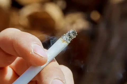 Dłoń trzymająca zapalonego papierosa, z którego unosi się dym. Zastanawiasz się, jak usunąć zapach papierosów ze ścian?