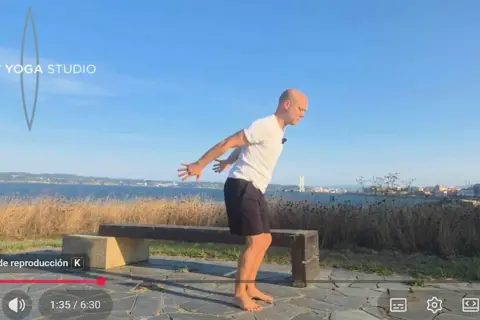 Hombre practicando yoga tibetano al aire libre, con el mar y la ciudad de fondo.