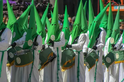 Nazarenos con túnicas blancas y capirotes verdes desfilan en la ruta cofrade Zaragoza, tambores resonando.