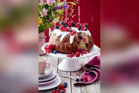 Ein köstlicher Gugelhupf mit Mandeln, Beeren und Zuckerguss, dekoriert mit frischen Früchten.