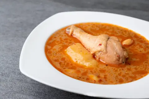En vit skål med en kycklingklubba och potatis i en krämig, kryddig sås. En härlig chicken massaman.