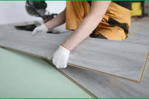 Manos enguantadas instalando suelos gran formato de madera gris.