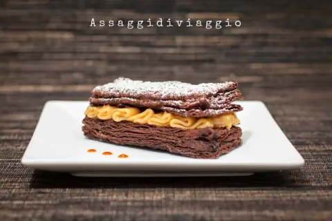 Un goloso millefoglie al cioccolato, con strati croccanti e crema dorata, spolverato di zucchero a velo.