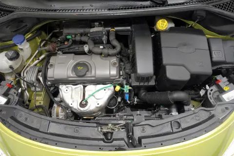 Silnik peugeot 207 1.4 benzyna. Widok komory silnika z widocznymi elementami, takimi jak alternator, obudowa filtra powietrza i zbiorniczek płynu chłodniczego.