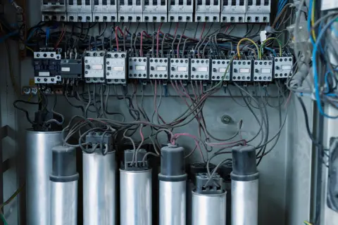 Wnętrze rozdzielnicy elektrycznej z kondensatorami i stycznikami, kluczowe dla poprawy współczynnika mocy cos fi.