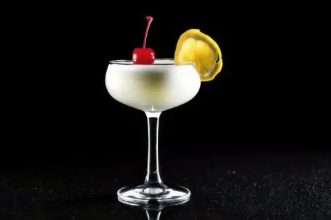 En elegant drink, en "white lady", med körsbär och citronskiva på svart bakgrund.