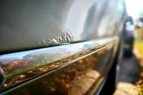 Nahaufnahme von Rostblasen am Auto, die eine Rostbehandlung am Auto erfordern.