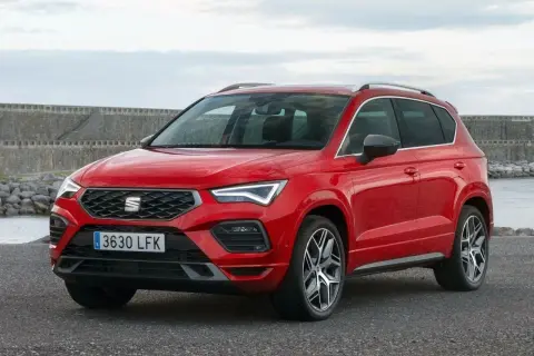 Czerwony Seat Ateca z nowoczesnymi światłami LED stoi na tle kamiennego nabrzeża i spokojnej wody.