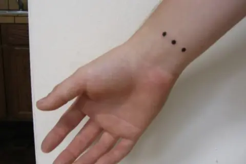 Muñeca con un discreto tatuaje de tres puntos negros alineados.