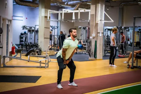 Man utför ett helkroppspass på gym med kettlebell.