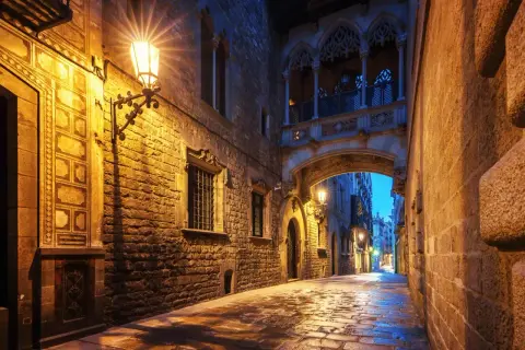 Calle empedrada y húmeda bajo un puente gótico iluminado, un rincón de los secret places Barcelona.
