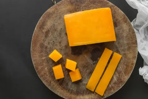 Un bloque de queso color naranja, cortado en cubos y bastones, sobre una tabla de madera.