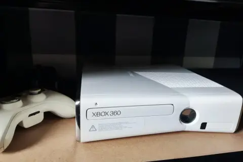 Biała konsola Xbox 360 i kontroler na półce.
