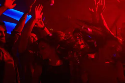 Leute tanzen ausgelassen im Club, die Haare fliegen, Konfetti fällt. Perfekt für eine **2000er Hits playlist**.