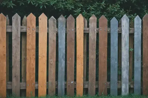 Różnobarwne, drewniane deski tworzą urokliwe, lekko zniszczone ogrodzenie. Jakie ogrodzenie, takie życie!