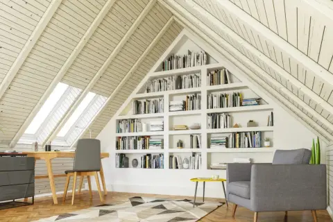 Gemütlicher Arbeitsplatz mit Bücherregalen im Dachausbau. Ein Schreibtisch unter Dachfenstern und eine Leseecke laden zum Verweilen ein.