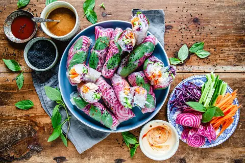 Färgglada vietnamesiska vårrullar med grönsaker och risnudlar, serverade med dippsåser och färska örter på en träbakgrund.