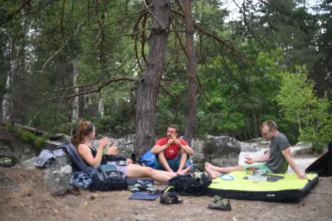 Drei Kletterer machen eine Pause im Wald von Fontainebleau. Ein Mann isst, während die anderen sich ausruhen.