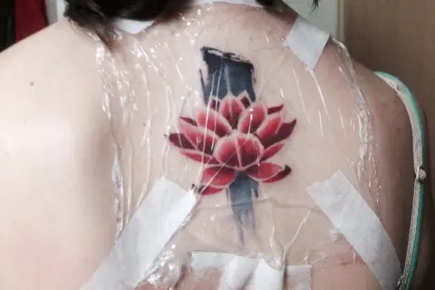 Flor de loto roja y azul recién tatuada en la espalda, cubierta con plástico y cinta. Preguntándose cuanto tarda en cicatrizar un tatuaje.