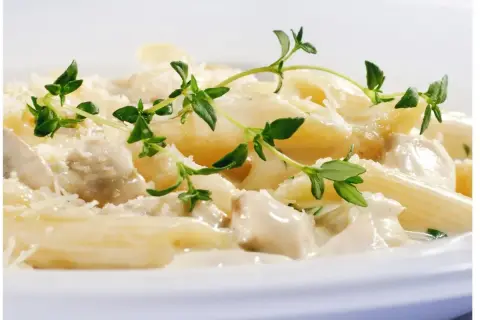 Penne z kurczakiem w kremowym sosie jogurtowym, posypane parmezanem i udekorowane gałązkami tymianku.