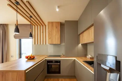 Cuisine moderne avec home staging réussi, mêlant bois chaleureux et finitions grises élégantes. L'îlot central en bois et les suspensions créent une ambiance accueillante.