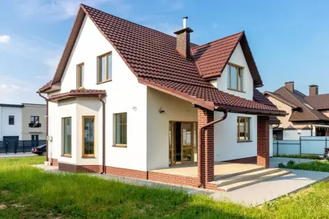 Biały dom z brązowym dachem i ceglanym cokołem. Elewacja w jasnych odcieniach to jedne z najmodniejszych kolorów elewacji, idealnie komponujące się z zielenią.