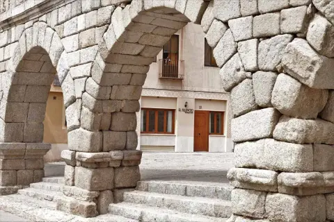 Arcos de piedra del Acueducto de Segovia, un lugar imprescindible que ver en Segovia. Al fondo, la fachada de un edificio con el letrero "El Silencio".