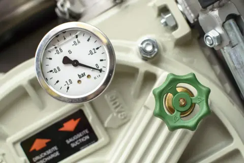 Manomètre indiquant la pression sur un appareil industriel, avec une valve verte et une étiquette "SAUGSEITE SUCTION". Ce **reducteur de pression** est essentiel.