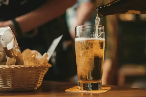 Złociste piwo IPA i APA leje się do szklanki. Obok koszyk z pieczywem.