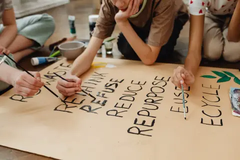 Niños pintan un cartel sobre la **competencia ciudadana LOMCE** y el reciclaje: "RETHINK, REFUSE, REDUCE, REPURPOSE, REUSE, RECYCLE".