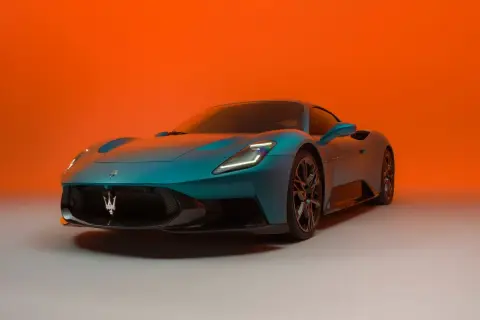Niebieski Maserati MC20 z charakterystycznym logo na grillu, prezentowany na tle pomarańczowego gradientu.