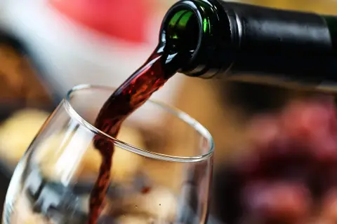 Mętne wino leje się z butelki do kieliszka. Ciemny płyn tworzy wiry, zapowiadając bogaty smak.