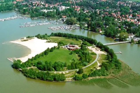 Grüne Insel mit Sandstrand und Gebäuden im Steinhuder Meer, umgeben von einem Yachthafen und einer Ortschaft.