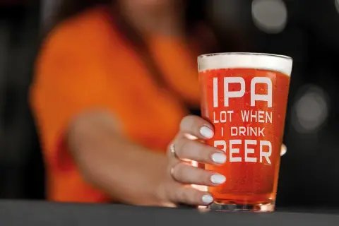 Un bicchiere di IPA con la scritta "IPA LOT WHEN I DRINK BEER" tenuto da una mano con unghie bianche.