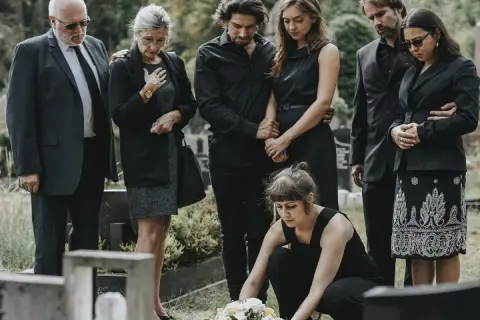 Famiglia in lutto, vestiti di nero per un funerale. Una donna depone fiori sulla tomba.