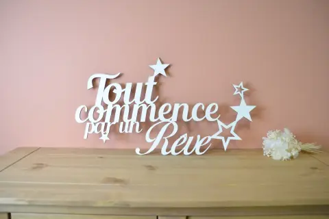 Une **lettre en bois blanc** forme la phrase "Tout commence par un Rêve", ornée d'étoiles. Un petit bouquet de fleurs séchées est posé à droite.