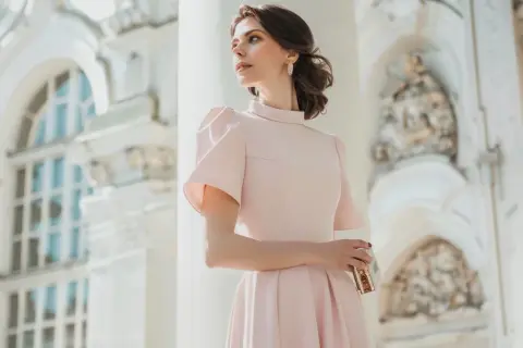 Elegancka kobieta w pudrowej sukience, idealna inspiracja, jak się ubrać na chrzciny jako gość kobieta.