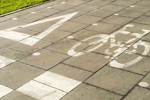 Un carril bici pintado sobre un **damero carretera** de baldosas grises. Una flecha blanca indica la dirección, seguida por el símbolo de una bicicleta.